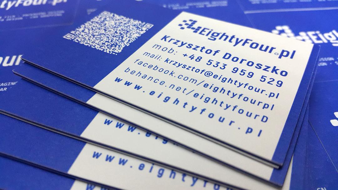 Stos wizytówek w kolorze niebieskim i białym, z danymi kontaktowymi firmy EightyFour.pl i kodem QR.