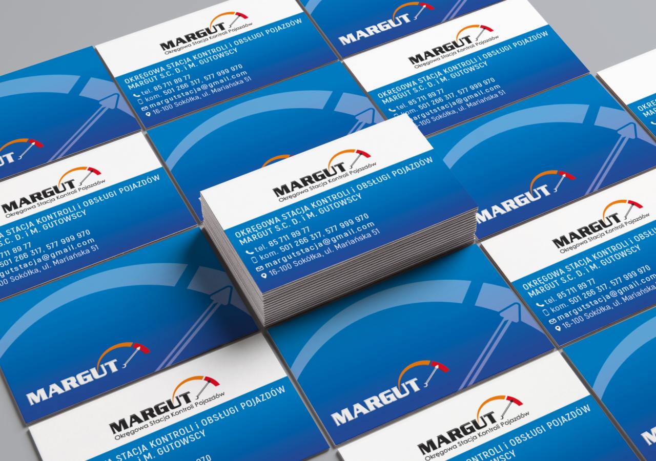 Stos wizytówek z logo i danymi kontaktowymi Okręgowej Stacji Kontroli Pojazdów Margut S.C. D. i M. Gutowscy, ułożonych na niebieskim tle.