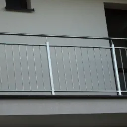 Barierka balkonowa ze stali nierdzewnej z pionowymi prętami, widok z zewnątrz, z oknem w tle.