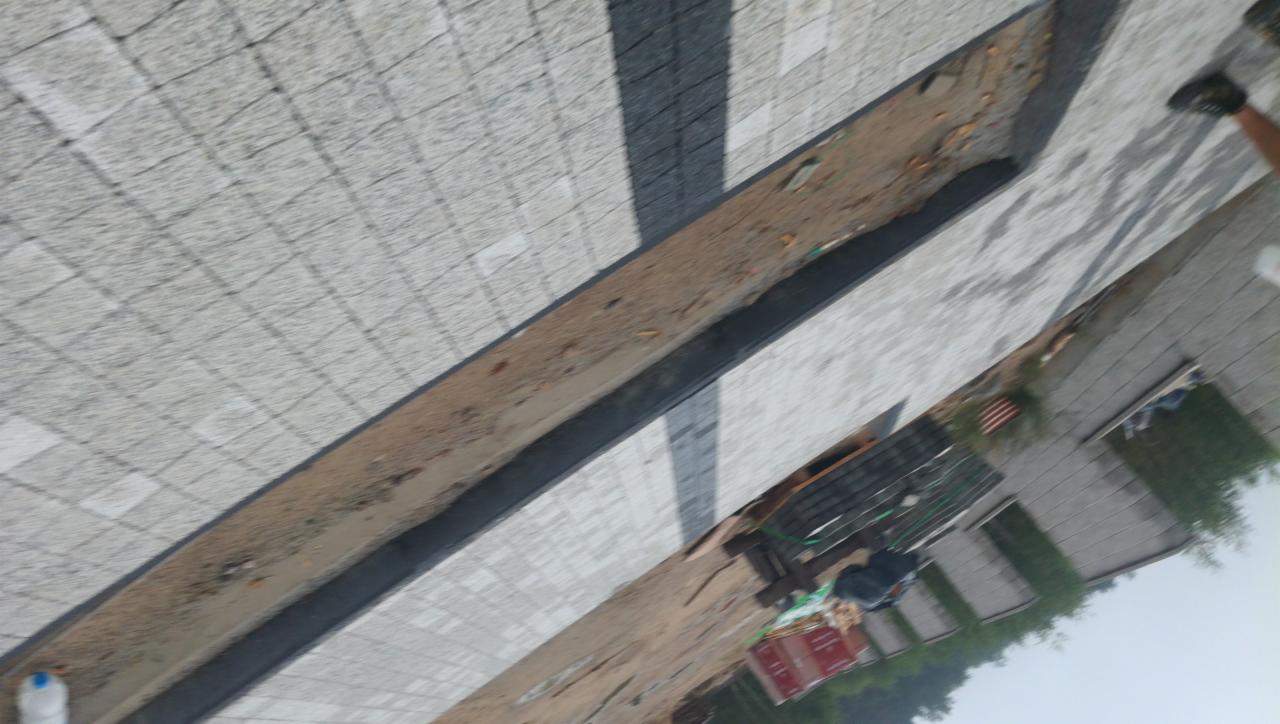 Świeżo ułożona, jasnoszara kostka brukowa z ciemniejszymi pasami, widoczny fragment buta osoby stojącej na boku, teren budowy w tle.