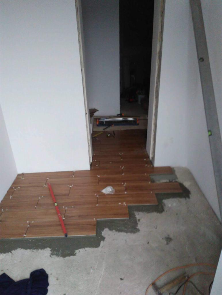 Fragment układania drewnopodobnych płytek na podłodze w przejściu, widoczny poziomica, płytki z krzyżykami dystansowymi, nieukończona powierzchnia.