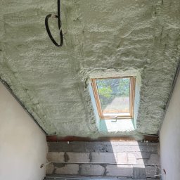 URB Kołakowski - Poddasze po ociepleniu pianką PUR, widoczne okno dachowe i instalacja elektryczna. Charakterystyczna struktura pianki na skośnym suficie.