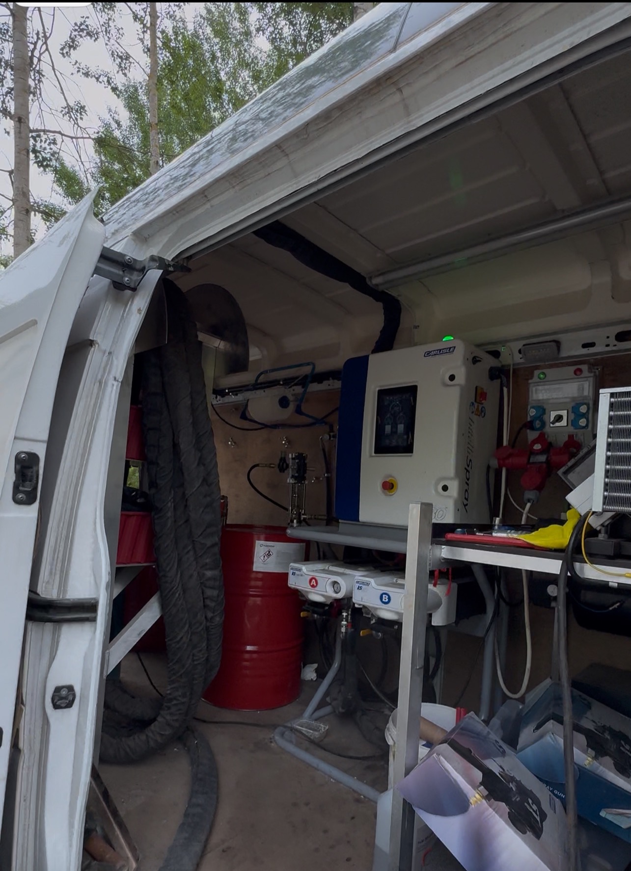 Wnętrze busa z maszyną Carlisle Spray Foam, czerwona beczka z komponentami. Sprzęt do natrysku pianki PUR gotowy do pracy w terenie.