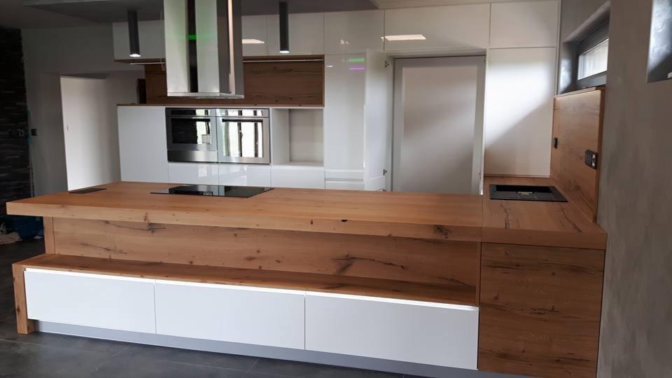 Nowoczesna kuchnia z wyspą i blatem z litego drewna o wyraźnym usłojeniu, w tle białe szafki i sprzęt AGD.