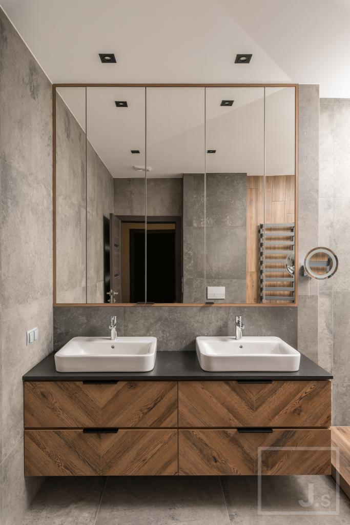 Nowoczesna łazienka z dwoma kwadratowymi umywalkami nablatowymi, szafką z drewnianym fornirem ułożonym w jodełkę i dużym lustrem z wbudowanym oświetleniem.