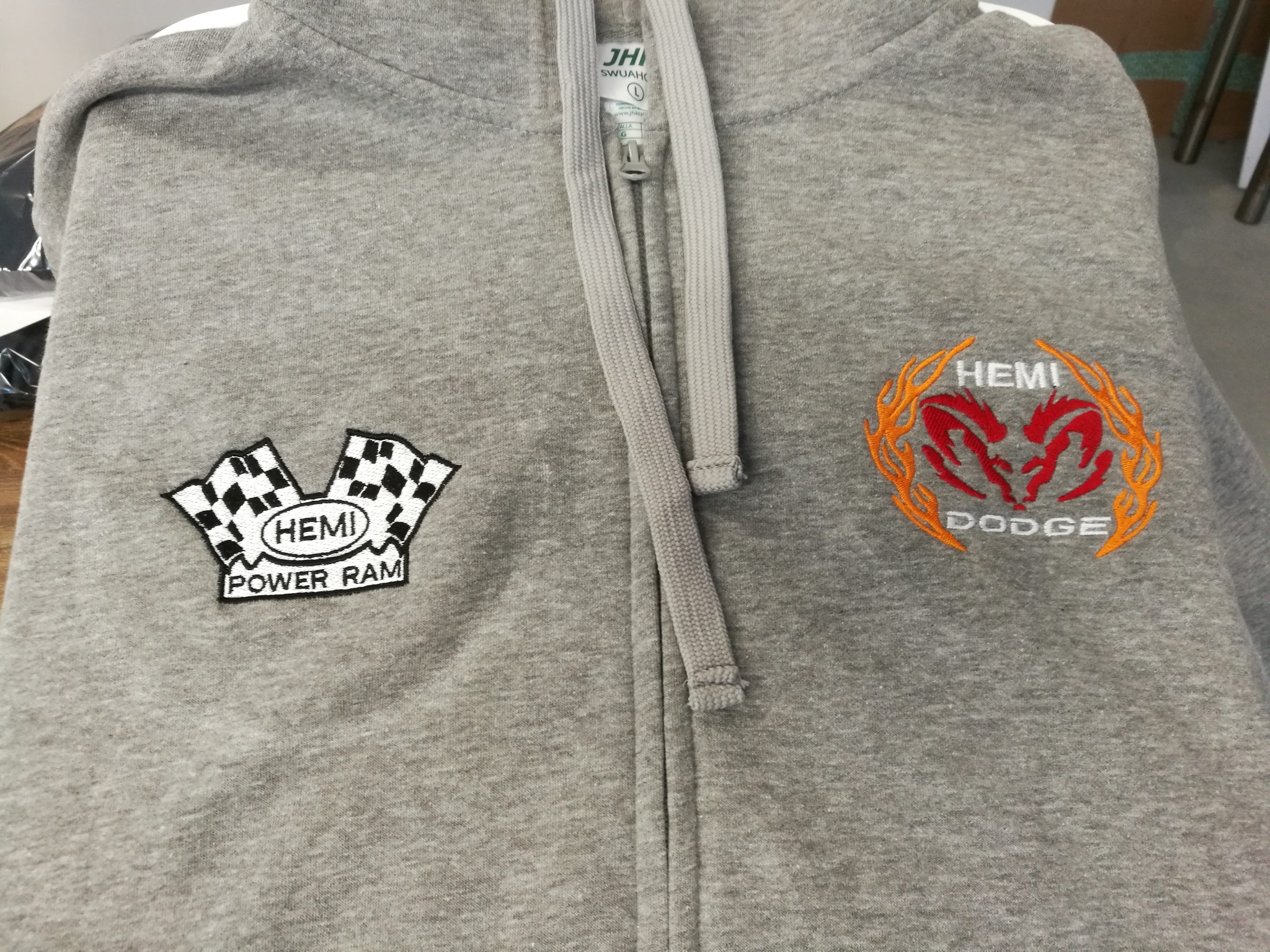Szara bluza z haftowanymi logotypami 'Hemi Dodge' i 'Power Ram' na klatce piersiowej. Bluza z suwakiem, widoczna metka i sznurki kaptura.