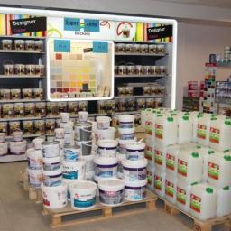 Budexpert - Wnętrze sklepu z farbami, prezentacja różnorodnych kolorów i pojemności, od małych puszek po duże pojemniki na paletach, na półkach ekspozycja z paletą barw i oznaczeniami cenowymi.