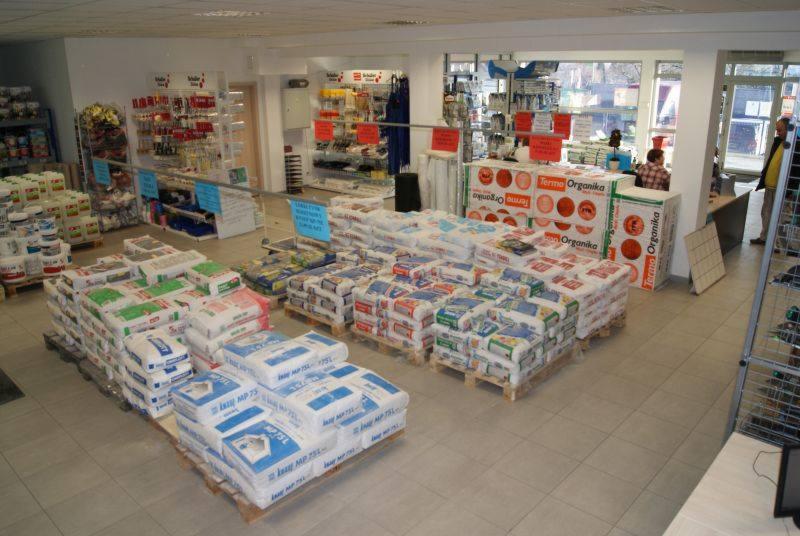 Wnętrze składu budowlanego z paletami worków zaprawy murarskiej Ixel MP 75L oraz materiałów ociepleniowych Terma Organika, widoczne regały z narzędziami i akcesoriami.