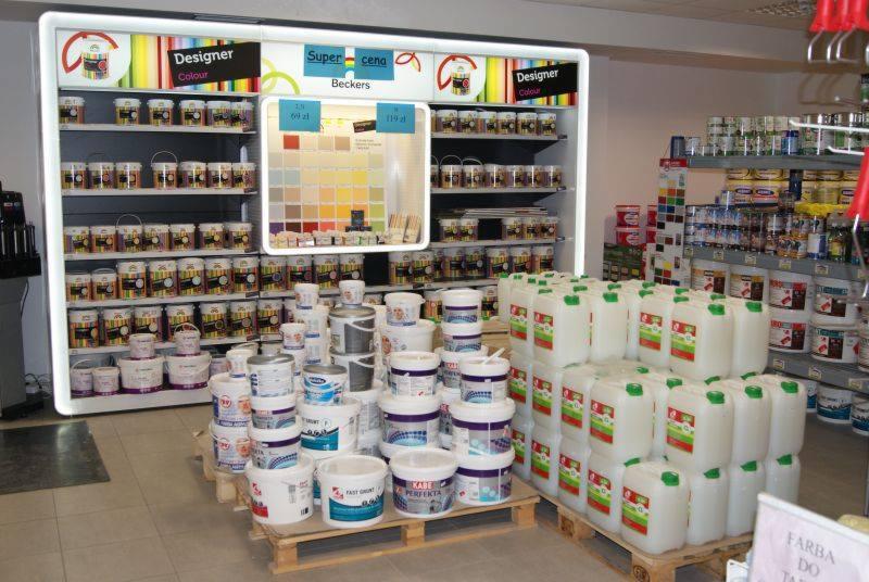 Wnętrze sklepu z farbami, prezentacja różnorodnych kolorów i pojemności, od małych puszek po duże pojemniki na paletach, na półkach ekspozycja z paletą barw i oznaczeniami cenowymi.