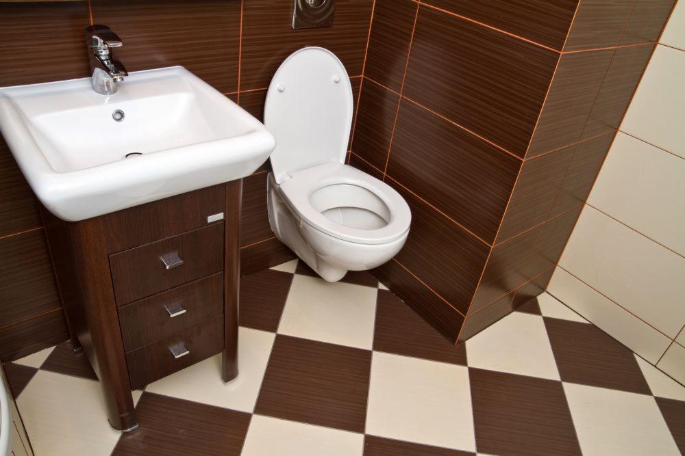 Umywalka z szafką z trzema szufladami i toaleta w łazience wykończonej brązowo-białymi płytkami w szachownicę, Ostrów Wielkopolski.