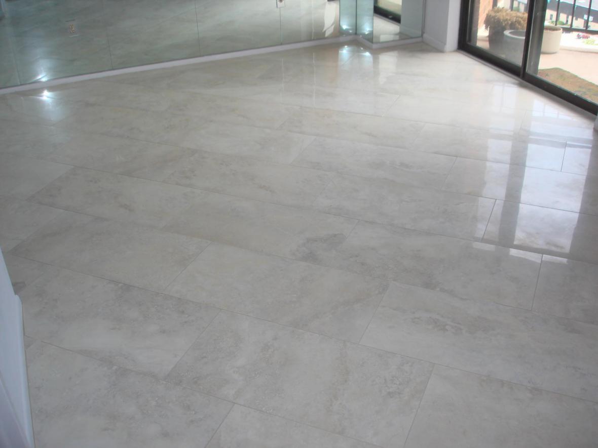 Jasne, polerowane płytki podłogowe ułożone w salonie z lustrzaną ścianą i oknem balkonowym.