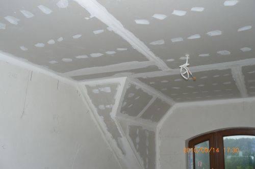 Sufit podwieszany z płyt kartonowo-gipsowych w trakcie montażu, widoczne łączenia szpachlowane, wystające przewody elektryczne, skos dachu.