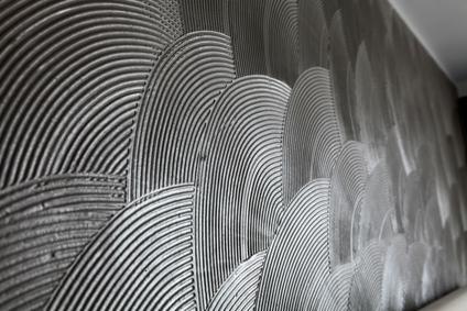 Dekoracyjna ściana z szarym tynkiem strukturalnym ułożonym w półokręgi, widoczne ślady pędzla i faktura materiału.