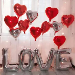 Dekoracja walentynkowa: srebrne litery układające się w słowo LOVE oraz czerwone i srebrne balony w kształcie serc na tle okna.