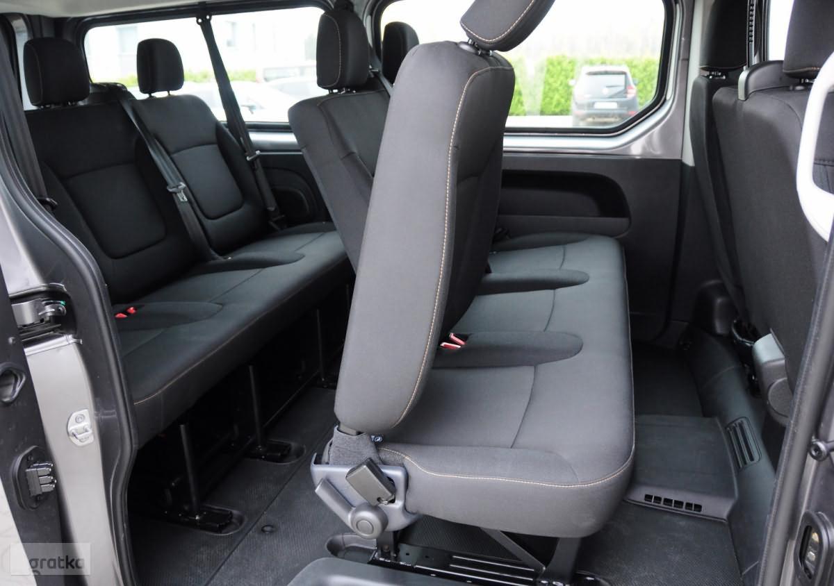 Wnętrze busa z trzema rzędami czarnych foteli z jasnymi przeszyciami, widok z otwartych tylnych drzwi na przestrzeń pasażerską.