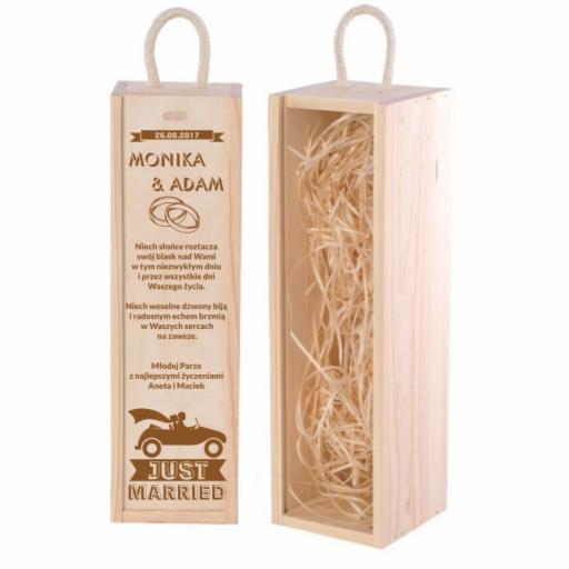 Drewniane pudełko na wino z grawerem imion Monika i Adam oraz datą ślubu 26.08.2017, ozdobione napisem 'Just Married' i rysunkiem pary młodej w samochodzie, wypełnione wiórkami.