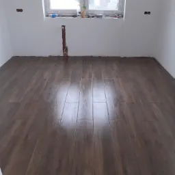 Ułożone panele podłogowe w odcieniach ciemnego drewna w pustym, świeżo wyremontowanym pokoju z białymi ścianami i oknem.