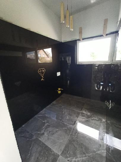 Nowoczesna łazienka z czarnymi, błyszczącymi panelami ściennymi i marmurową podłogą w odcieniach szarości, oświetlona wiszącymi lampami tubowymi.