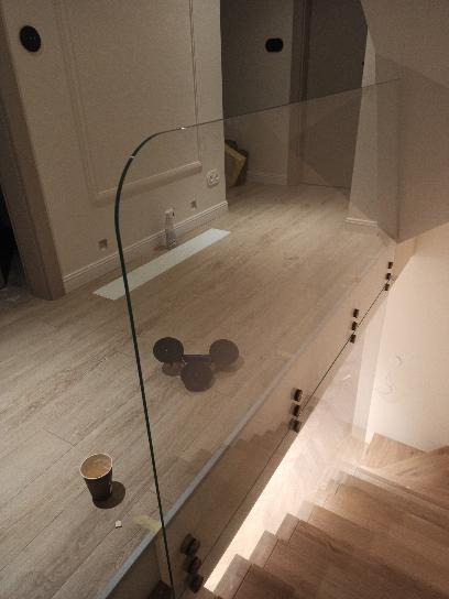 Szklana balustrada na schodach z drewnianymi stopniami, widoczne mocowania punktowe, na podłodze kubek po kawie i zabawka.