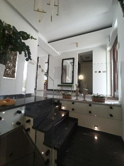 Nowoczesne schody wykończone czarnym marmurem z balustradą ze szkła bezramowego, oświetlenie punktowe w stopniach i podestach, widok z dołu na przestronny hol z lustrem i dekoracjami.