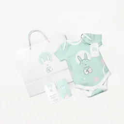 Zestaw materiałów firmowych Kraina Bo: torba papierowa z logo, wizytówki oraz niemowlęce body z nadrukiem logo na jasnym tle.