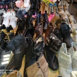 Różnorodny asortyment używanych butów: kozaki, botki, adidasy, półbuty, widoczne ślady użytkowania, ustawione na stole w sklepie z odzieżą używaną.