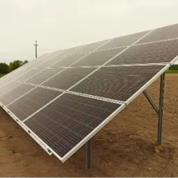 Instalacja paneli słonecznych na polu, widoczne metalowe konstrukcje wsporcze i horyzont z drzewami pod pochmurnym niebem.