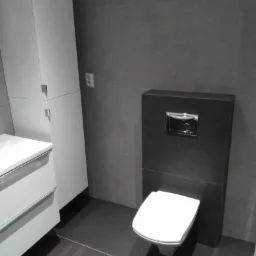 Szara łazienka z podwieszaną toaletą, białą szafką z umywalką i ciemną podłogą z płytek.