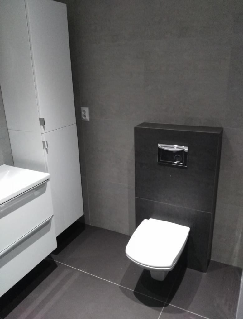 Szara łazienka z podwieszaną toaletą, białą szafką z umywalką i ciemną podłogą z płytek.