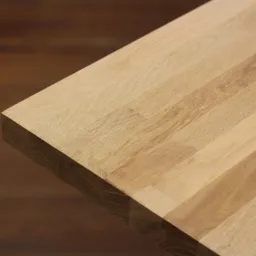 Fragment blatu z jasnego drewna klejonego warstwowo, widoczne łączenia i usłojenie, na rozmytym tle w odcieniach brązu.