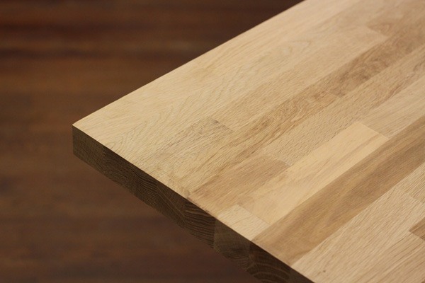 Fragment blatu z jasnego drewna klejonego warstwowo, widoczne łączenia i usłojenie, na rozmytym tle w odcieniach brązu.