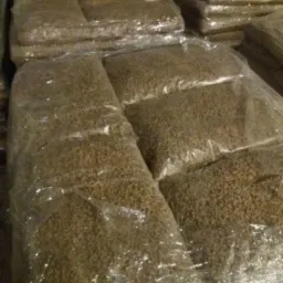 Ułożone palety worków z pelletem, zapakowane w przezroczystą folię, widoczne w słabym oświetleniu magazynu.