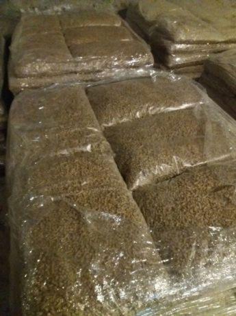 Ułożone palety worków z pelletem, zapakowane w przezroczystą folię, widoczne w słabym oświetleniu magazynu.