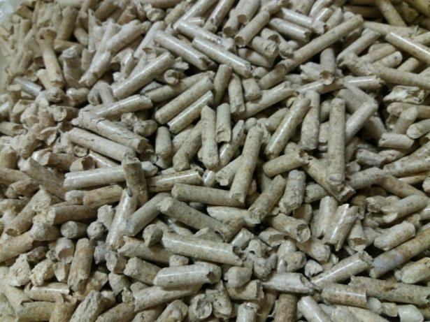 Stos jasnych, drewnianych pelletów opałowych z widoczną strukturą włókien drzewnych i niewielkimi uszkodzeniami mechanicznymi.