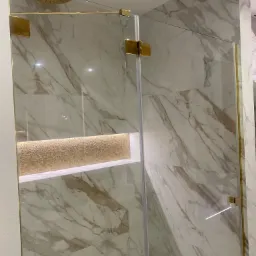 Nowoczesna kabina prysznicowa z marmurowymi płytkami, złotymi okuciami i deszczownicą, podświetlana wnęka z mozaiką.