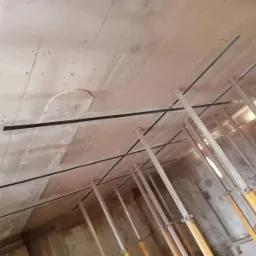 Betonowy strop z widocznymi czarnymi wzmocnieniami i podporami budowlanymi.