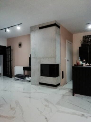 Nowoczesny, surowy w formie, betonowy element grzewczy z czarnymi akcentami, w przestronnym wnętrzu z marmurową podłogą i minimalistycznym oświetleniem.