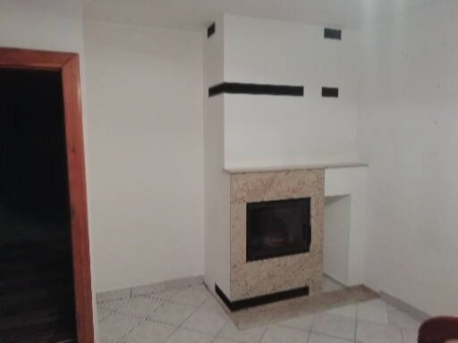 Nowoczesny wkład kominkowy obudowany beżowym kamieniem, z czarnymi akcentami, osadzony w białej ścianie z minimalistycznymi czarnymi elementami dekoracyjnymi.