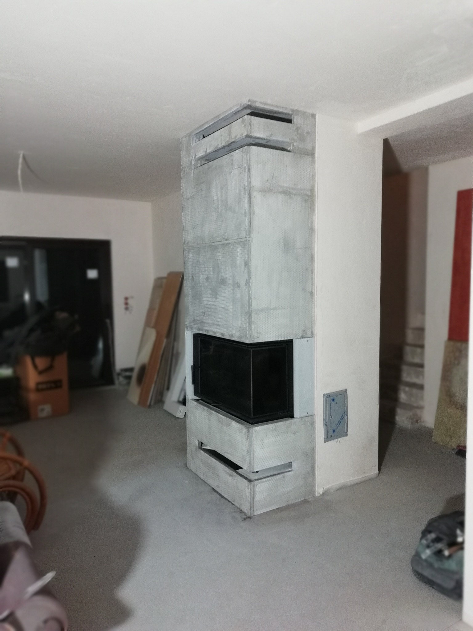 Nowoczesny, surowy kominek z szarego betonu w surowym wnętrzu. Widoczne niedokończone ściany i podłoga. Minimalistyczny design z czarnym wkładem.