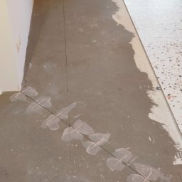 Tomasz Górski - Podłoga w trakcie układania płytek, widoczne sznurki i krzyżyki dystansowe, częściowo ułożone płytki lastryko, surowy beton pod spodem.