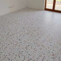 Tomasz Górski - Nowoczesna posadzka z płytek lastryko w jasnym wnętrzu, widok na ścianę z gniazdkami i okno balkonowe z widokiem na budynek.