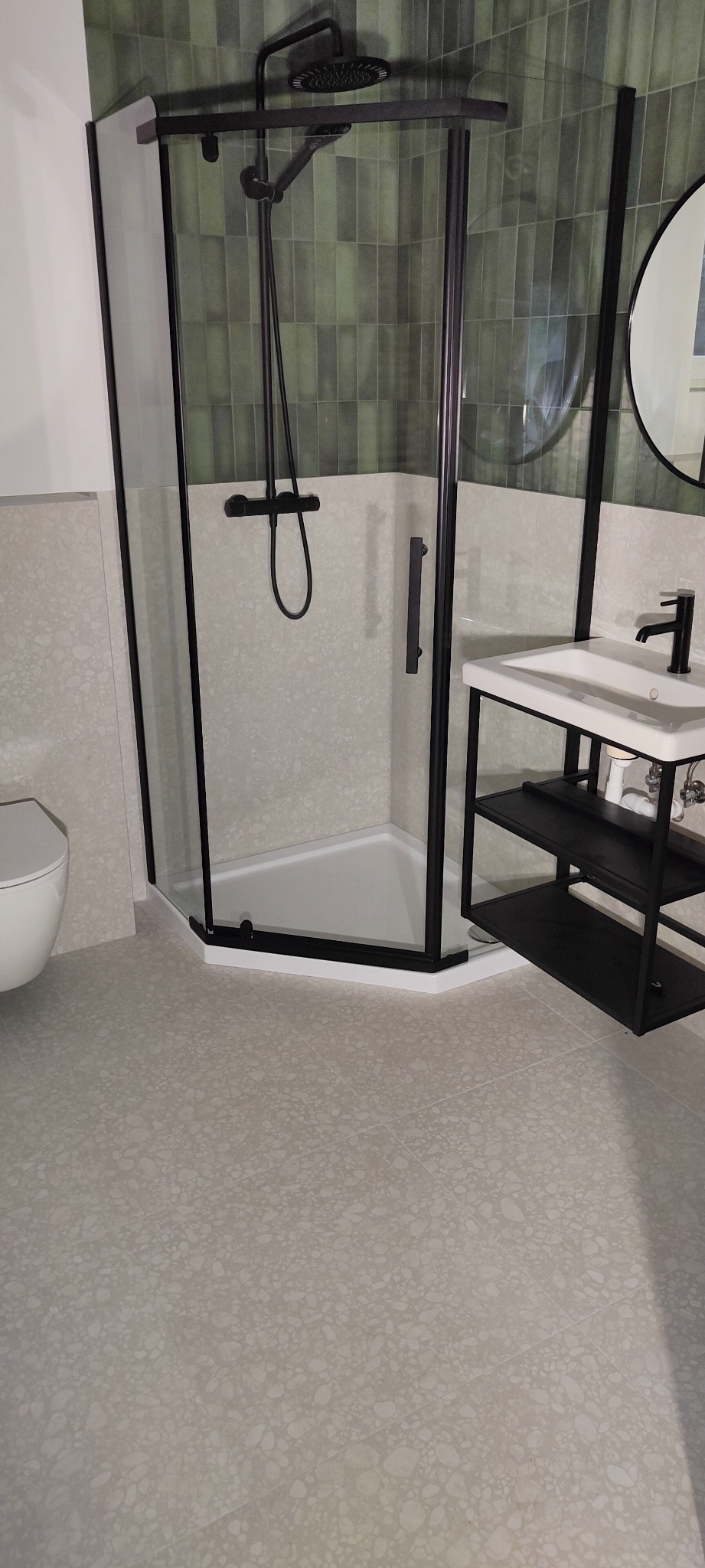 Nowoczesna łazienka z kabiną prysznicową z czarnymi profilami, umywalką na czarnym metalowym stelażu i zielonymi płytkami na ścianie