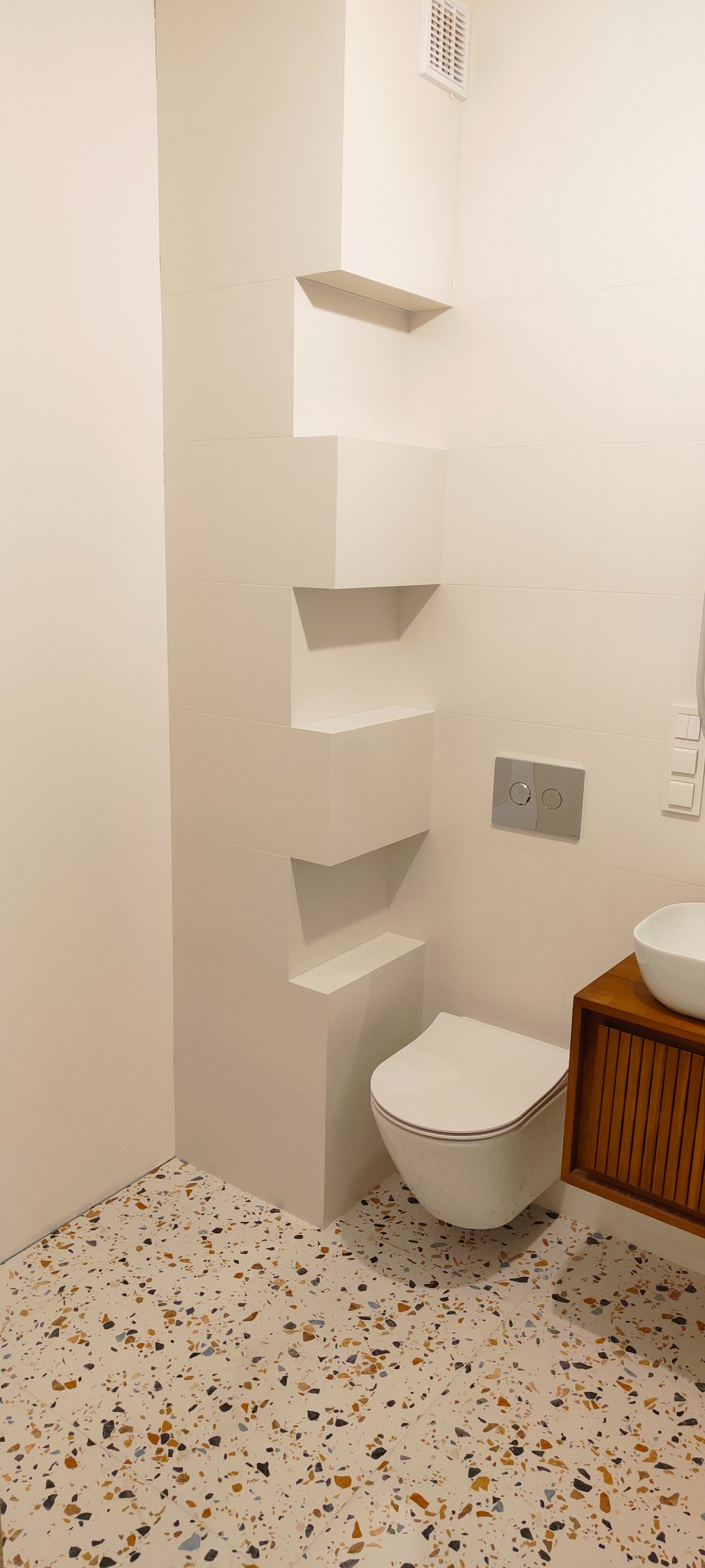 Nowoczesna łazienka w Żyrardowie z białymi płytkami, zabudową WC z półkami wnękowymi i posadzką lastryko.