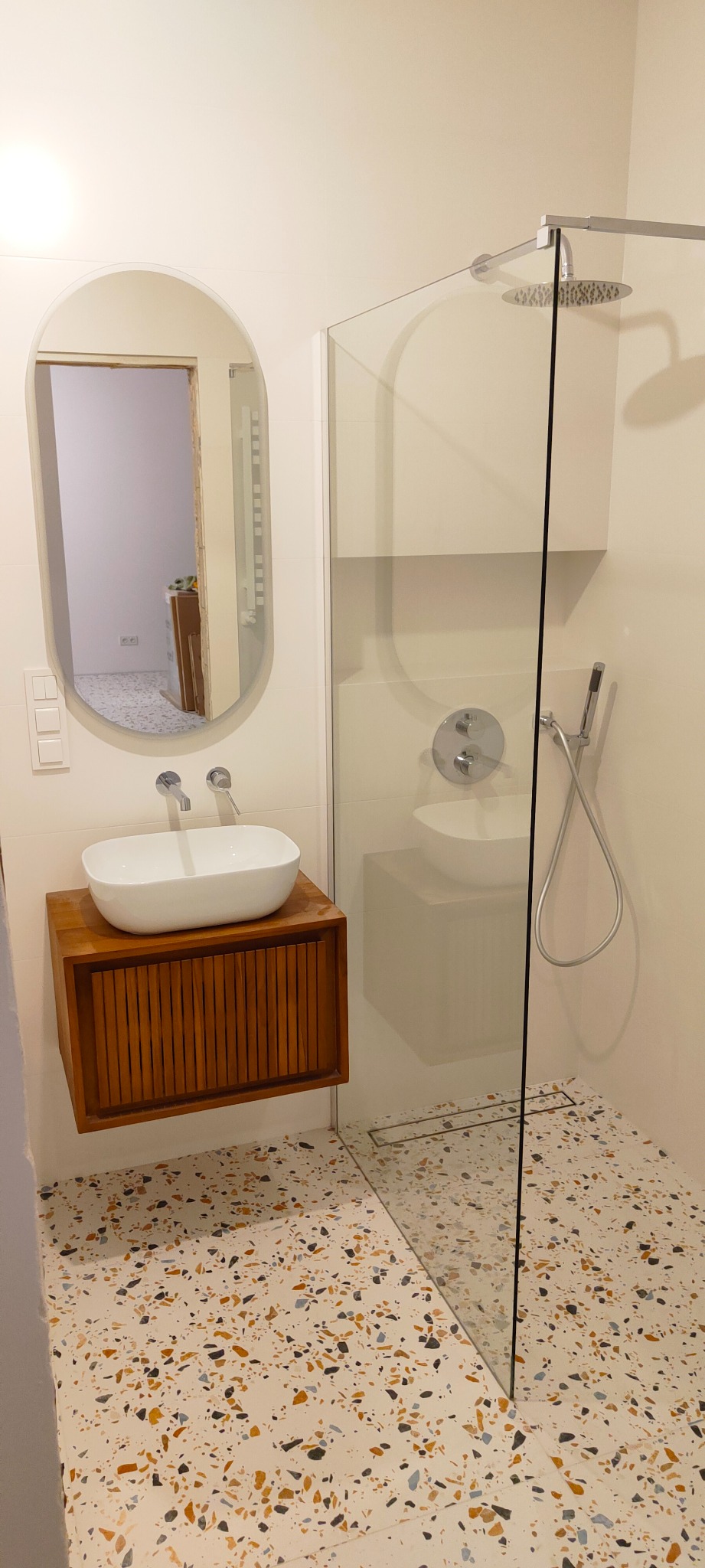 Nowoczesna łazienka z umywalką nablatową na drewnianej szafce, kabina prysznicowa typu walk-in z deszczownicą i odpływem liniowym oraz podłoga z lastryko.