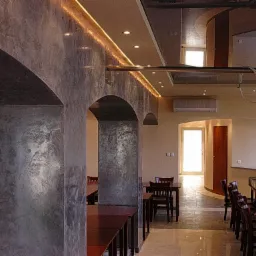 Wnętrze restauracji z dekoracyjnymi, szarymi kolumnami wykończonymi efektem stiuku weneckiego, oświetleniem LED podsufitowym i ciemnymi, drewnianymi meblami.