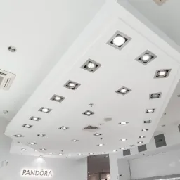 Sufit podwieszany w sklepie z oświetleniem punktowym w kwadratowych oprawach, klimatyzacja kasetonowa, białe ściany i logo Pandora.