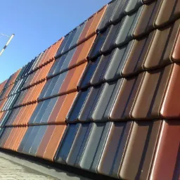 Ekspozycja dach&oacute;wek ceramicznych w r&oacute;żnych kolorach i odcieniach, ułożonych rzędami, z widocznym niebieskim niebem w tle i fragmentem konstrukcji reklamowej.