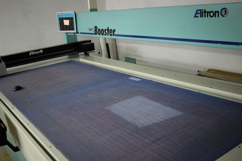 Automatyczna krajalnica Elitron Cut Booster z niebieskim materiałem tekstylnym na stole roboczym, widoczny panel sterowania i logo.