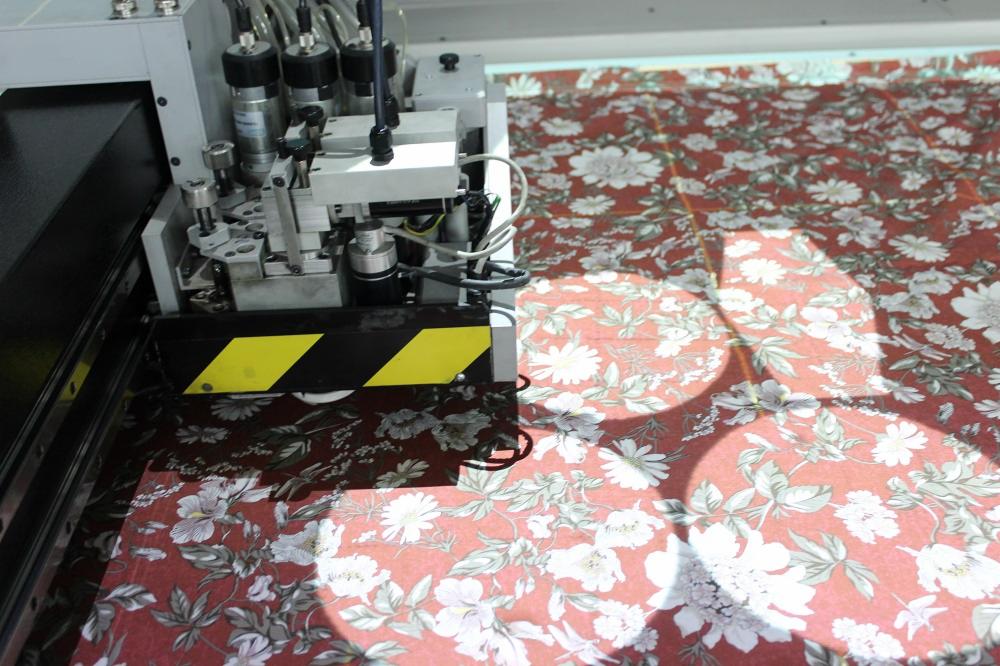 Automatyczna maszyna tnąca w Garwolinie precyzyjnie wycina wzór z tkaniny w kwiaty na tle jasnego blatu roboczego, widoczne przewody i elementy mechaniczne urządzenia.
