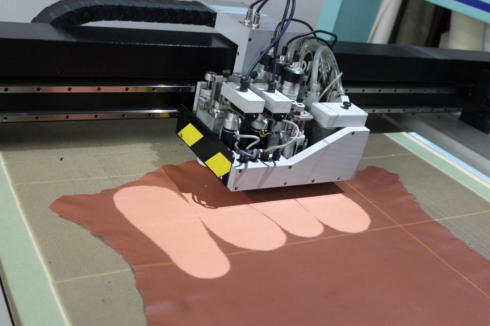 Automatyczna krojownia tnąca brązową skórę, widoczne przewody i elementy mechaniczne maszyny.